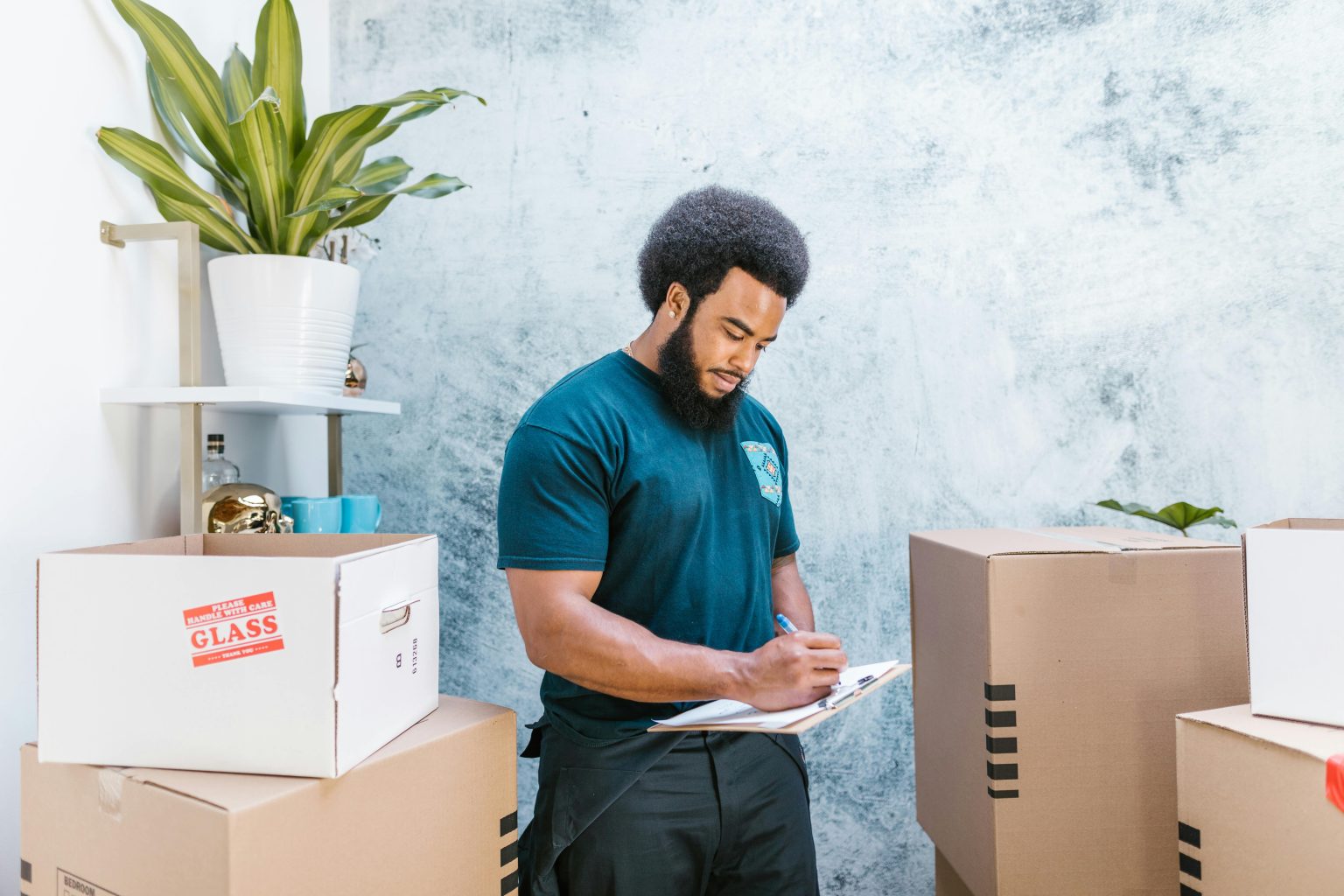 A mover with a clipboard checking packages and boxes for relocation indoors.