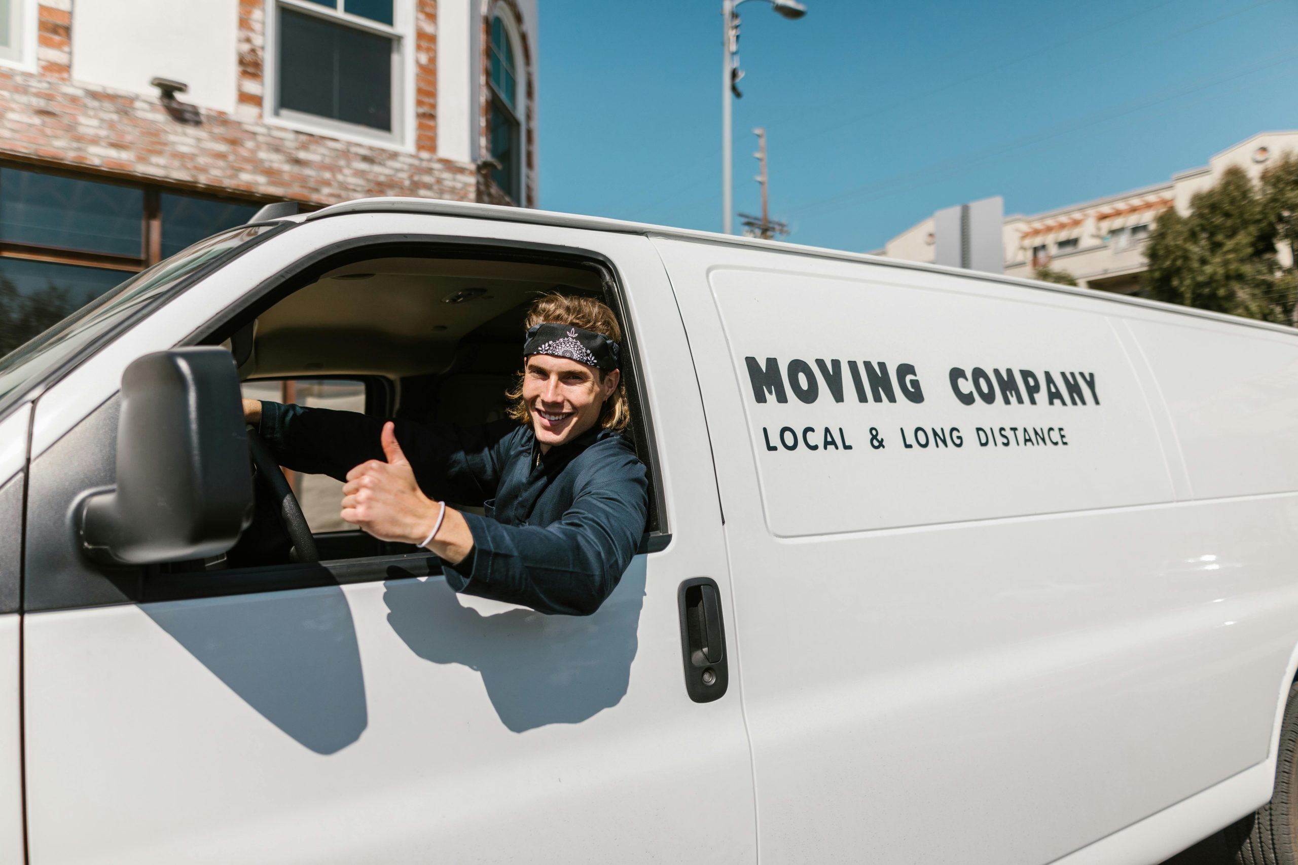 Smiling mover giving thumbs up from a moving company van parked outside.